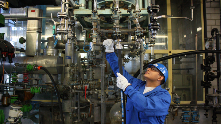 Arbeiter in blauer Schutzkleidung prüft Ventile in Industrieanlage.