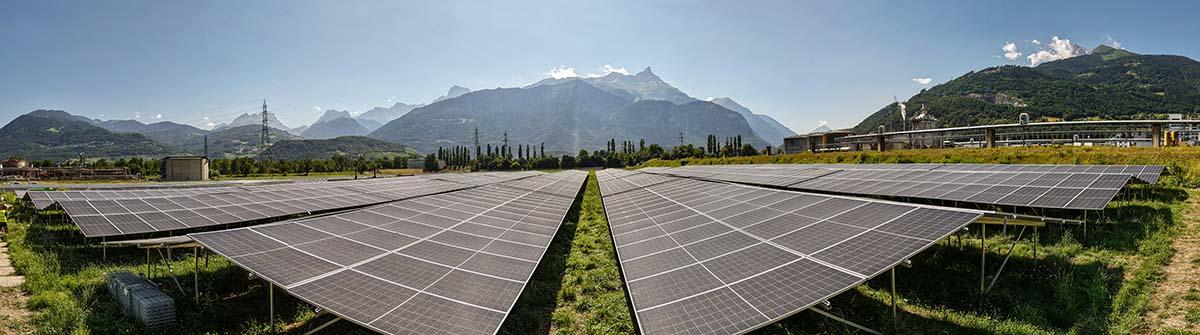 Große Solarfarm in grünem Tal vor Bergen unter blauem Himmel