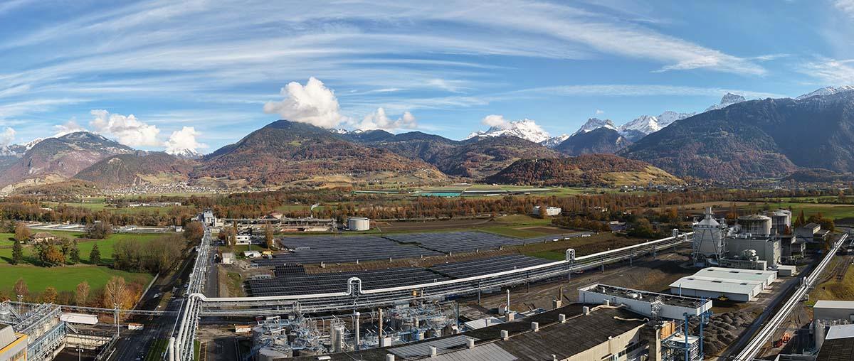 Luftaufnahme einer Industrieanlage vor Bergen und blauem Himmel